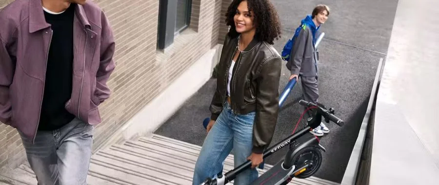 A woman carrying a folded Segway scooter up outdoor stairs.