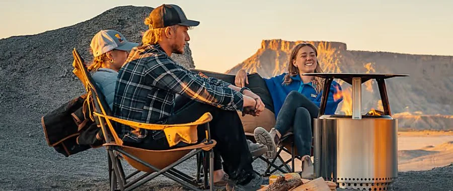 Three friends enjoying their Solo Stove and fire with the heat deflector outdoors near a canyon as the sun sets.
