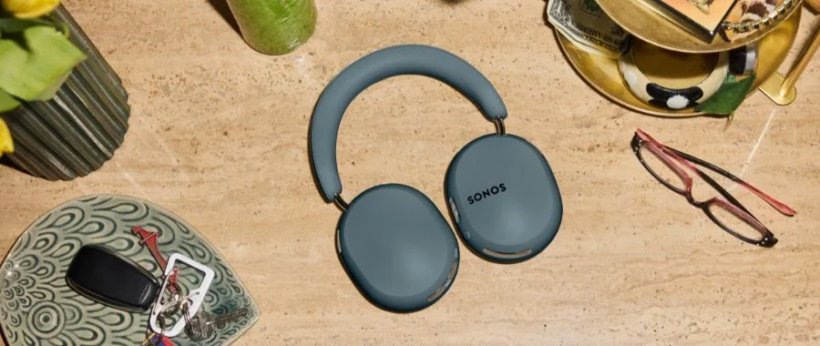 Flat lay of Sonos Ace Ultra headphones in agave next to glasses and a catchall tray.