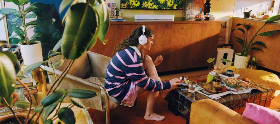Person in a striped shirt wearing white Sonos Ace Ultra headphones while applying toenail polish.