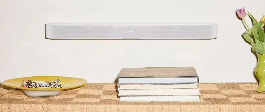 A white sonos beam ultra soundbar mounted to the wall above a table stacked with books