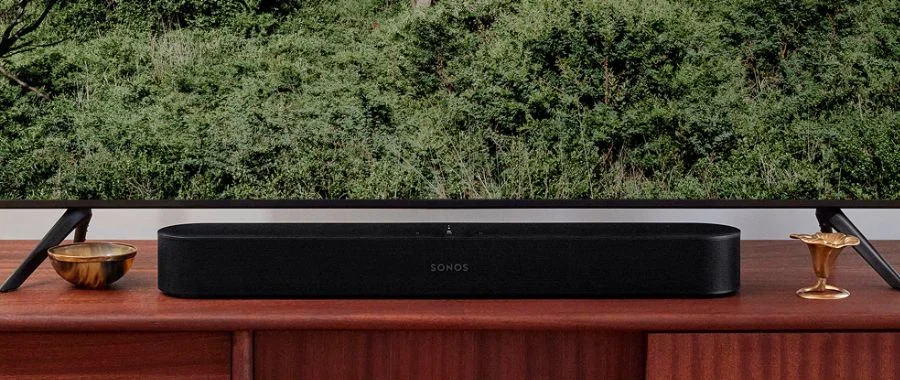 A black Sonos Beam soundbar on a wood TV stand under a TV,