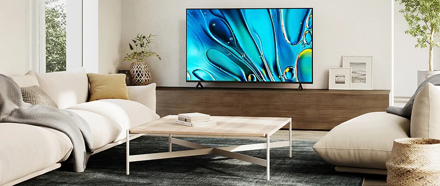 The Sony Bravia 3 sitting on a stand displaying blue art in a living room with two couches and a coffee table