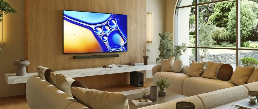 A Sony Bravia 8 II TV hung on the wall in a living room above a soundbar and surrounded by a large sectional.