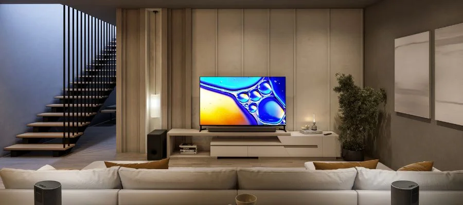 A Sony Bravia 8 II TV in front of a large sofa and beside a subwoofer and staircase.