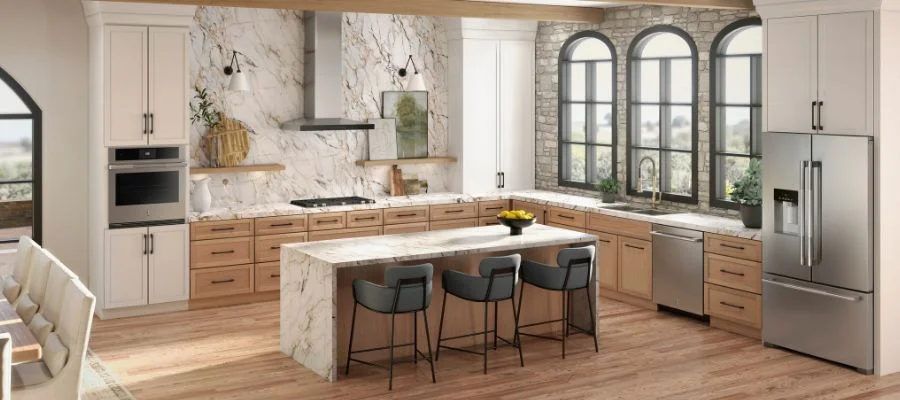 JennAir stainless steel refrigerator, dishwasher and wall oven in a kitchen with light wood cabinets and marble counters.