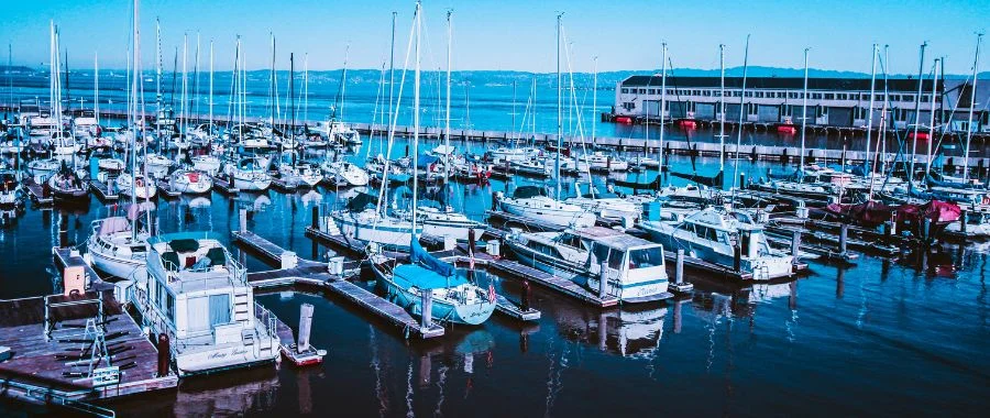 A variety of boats docked at a pier on clear, blue water.