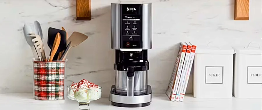 The Ninja Creami sitting on a white countertop next to a glass bowl of freshly made peppermint ice cream