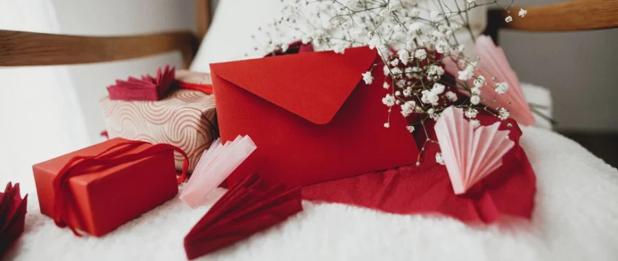 A small group of Valentine’s Day gifts, wrapped in red paper next to baby’s breath flowers and a red card.