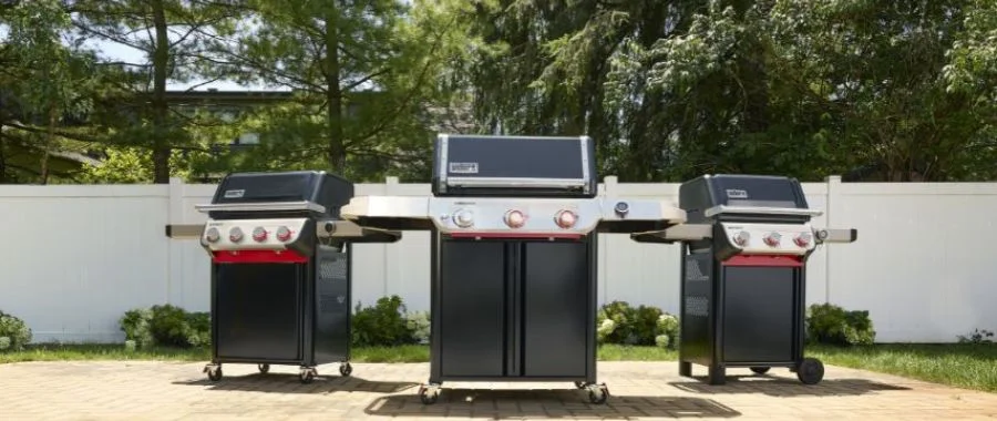 A black Weber Summit, Genesis and Spirit all outdoors on a patio on a sunny day