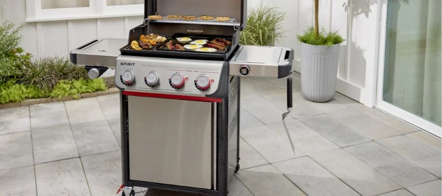 A four-burner stainless steel weber spirit grill with sizzling meats and veggies on the patio