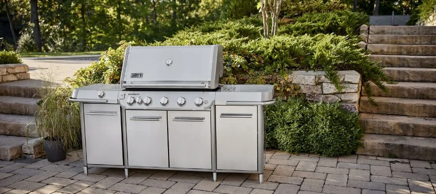 A five-burner stainless steel Weber Summit grill with two side tables and multiple cabinets outdoors on the patio.