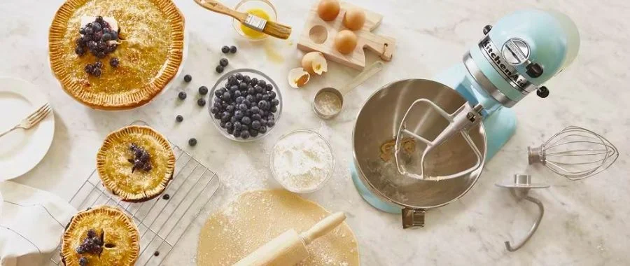 A light blue KitchenAid stand mixer using the paddle attachment to make blueberry pies.
