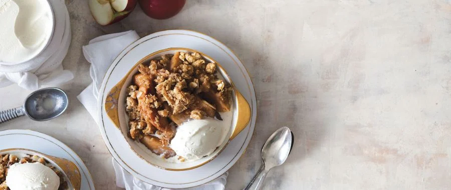 Wolf apple crisp recipe topped with a scoop of ice cream in a dish beside a spoon