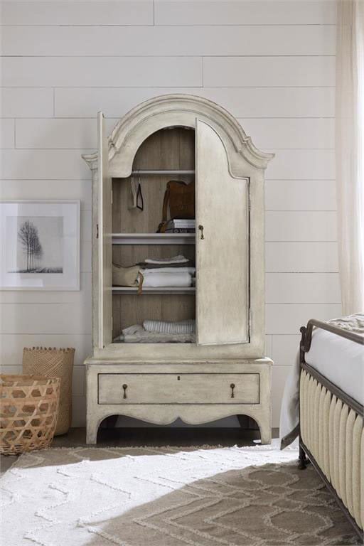 A white armoire in a bedroom with a bed and other furniture, open to show shelves with items