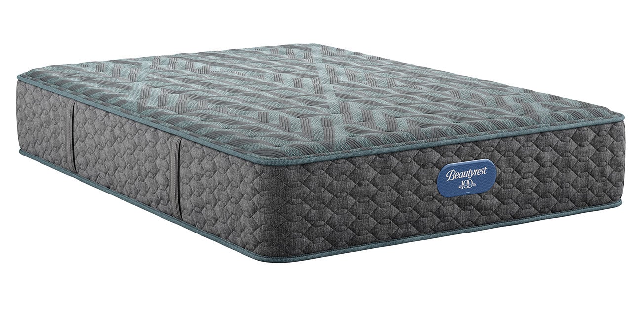 A close-up view of a gray quilted medium-support mattress with teal piping and a blue Beautyrest 100 label on the side.