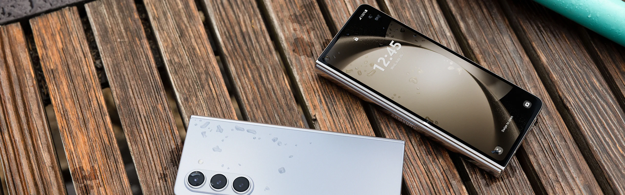 Two Samsung galaxy fold phones covered in water drops on a boardwalk