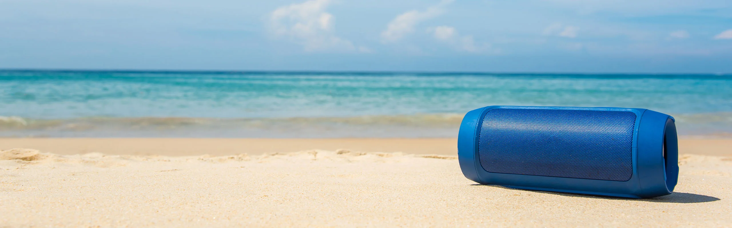 A Bluetooth Speaker Sitting on a Beach with Water in Background.
