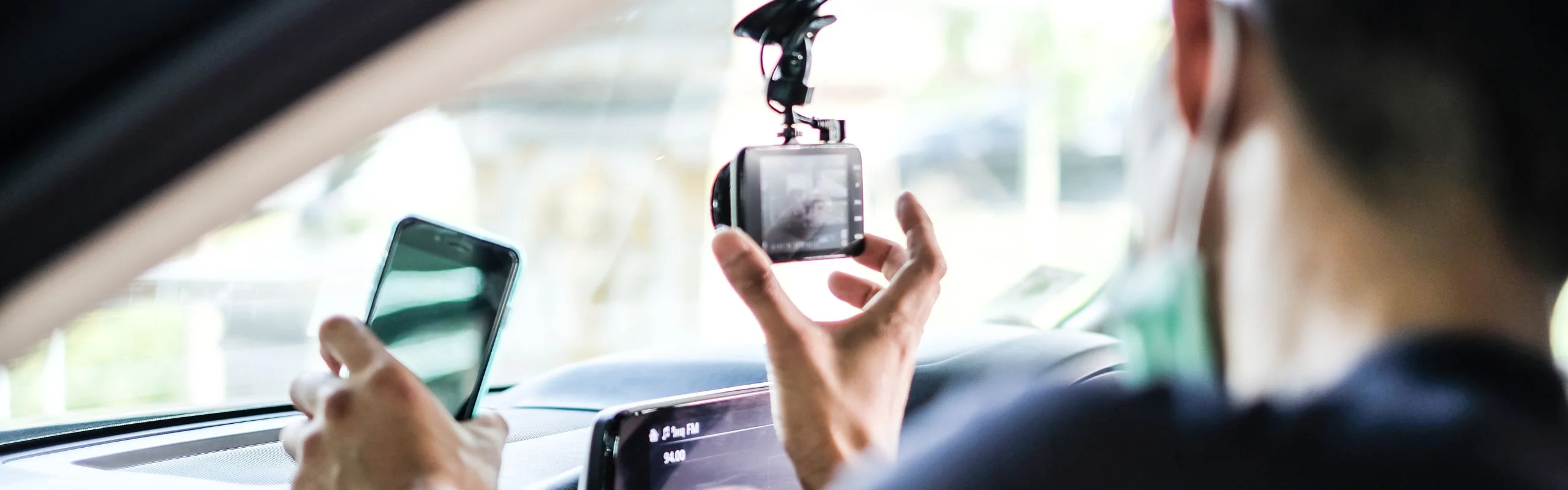 An image of a dash cam with an LCD screen being installed in a car, suction cupped to the window.