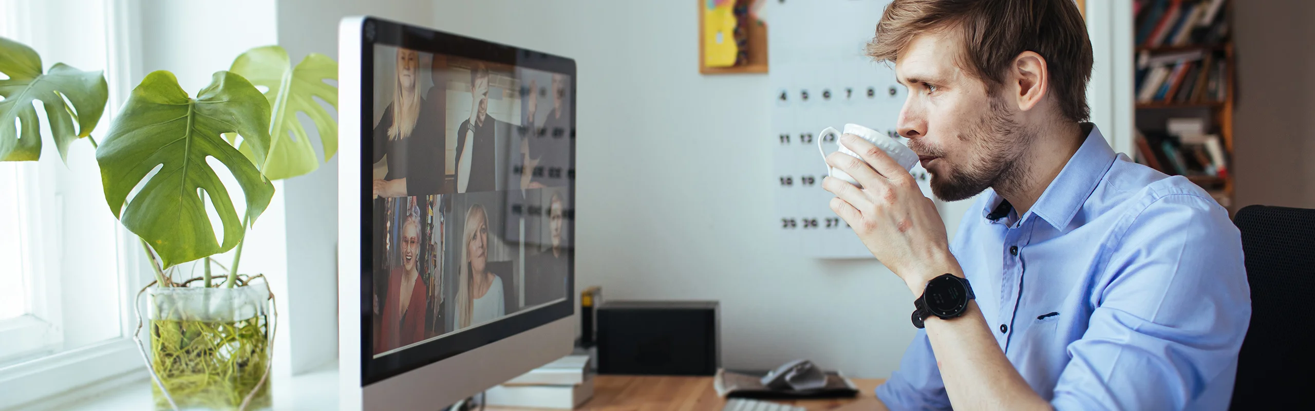 A man taking a sip of coffee in front of a computer screen with a group video call on it