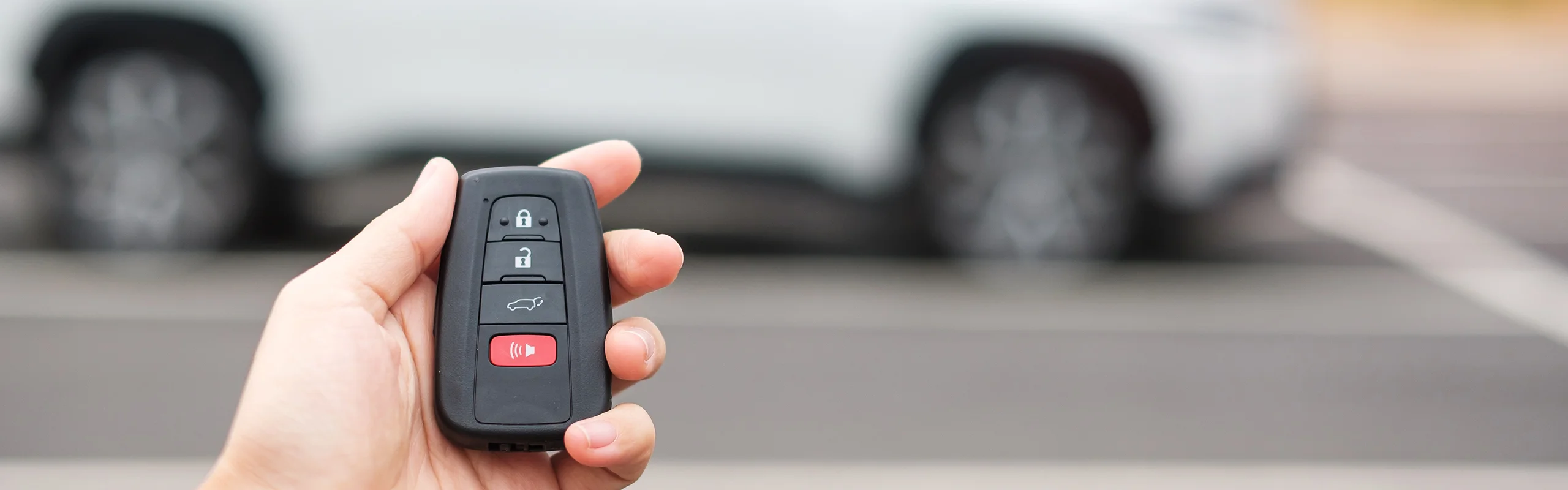 A hand holding a black car alarm fob with buttons to lock, unlock, pop the trunk and set off the alarm