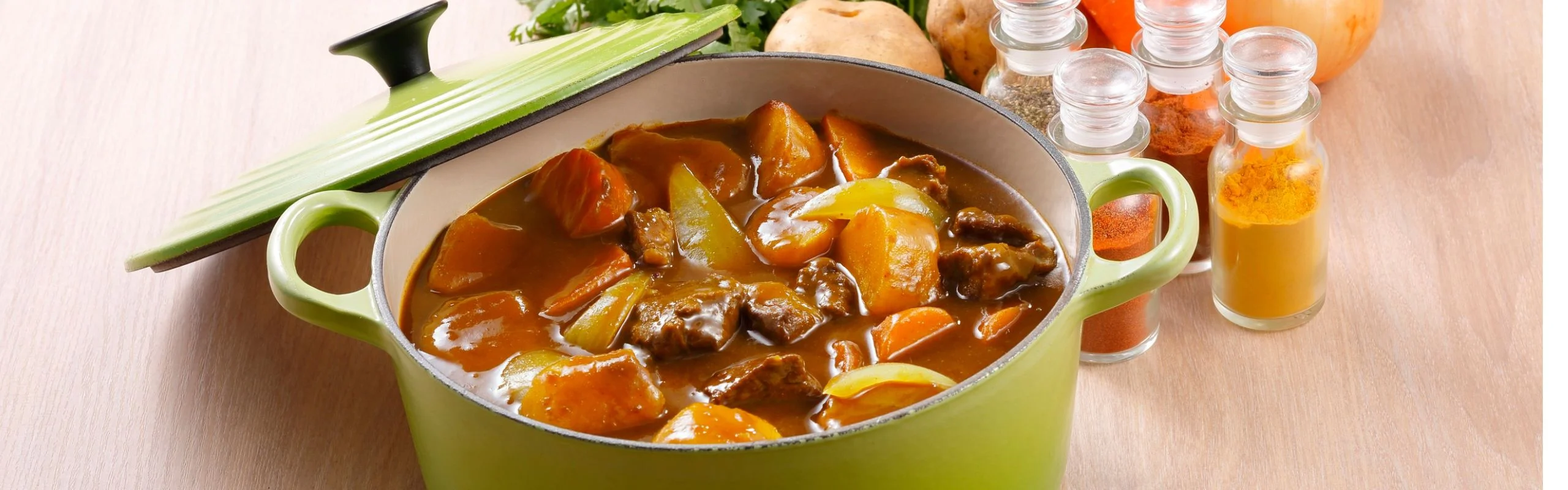 A green Dutch oven filled with a beef and carrot stew.