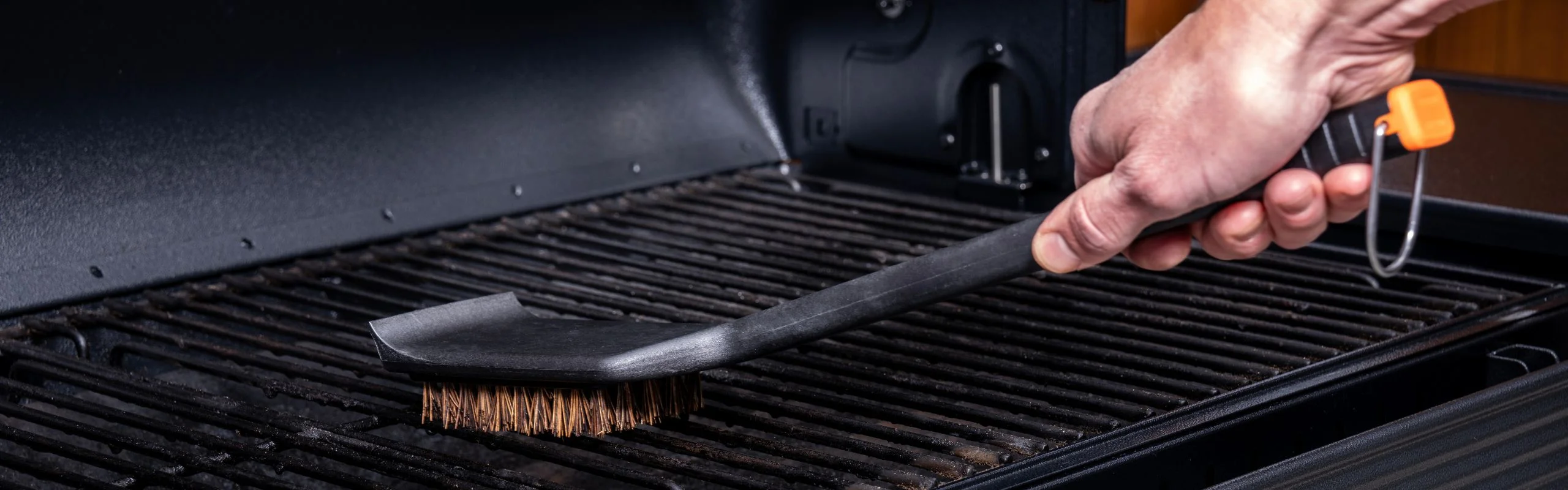 Closeup of person scrubbing grill grates with a black grill brush.