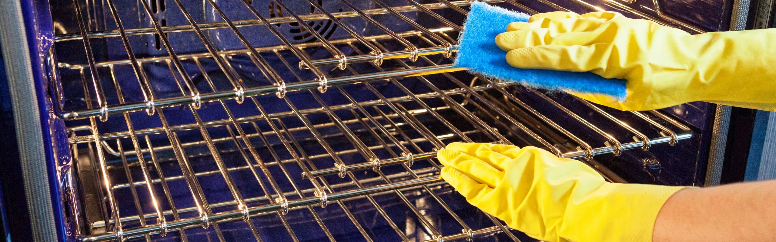 Gloved hands cleaning the inside of an oven with a sponge