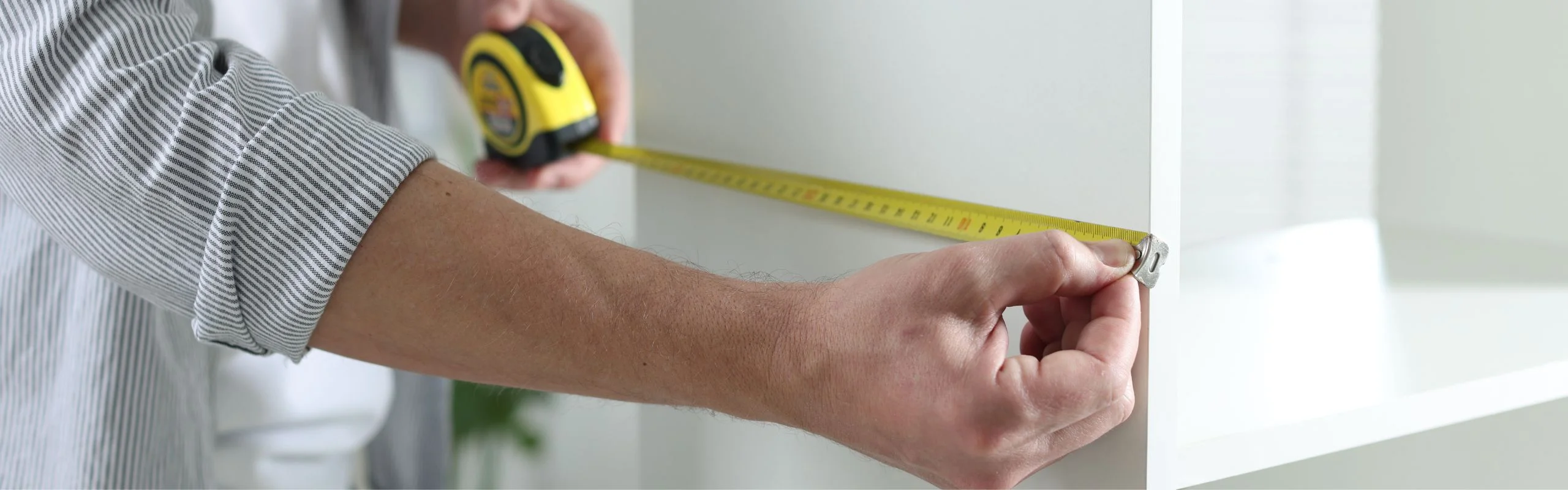 A man with rolled-up sleeves measuring a bookshelf with a tape measure