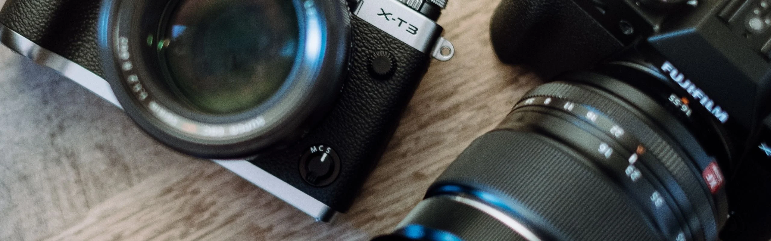 A DSLR and a mirrorless camera placed on a wooden table side-by-side.