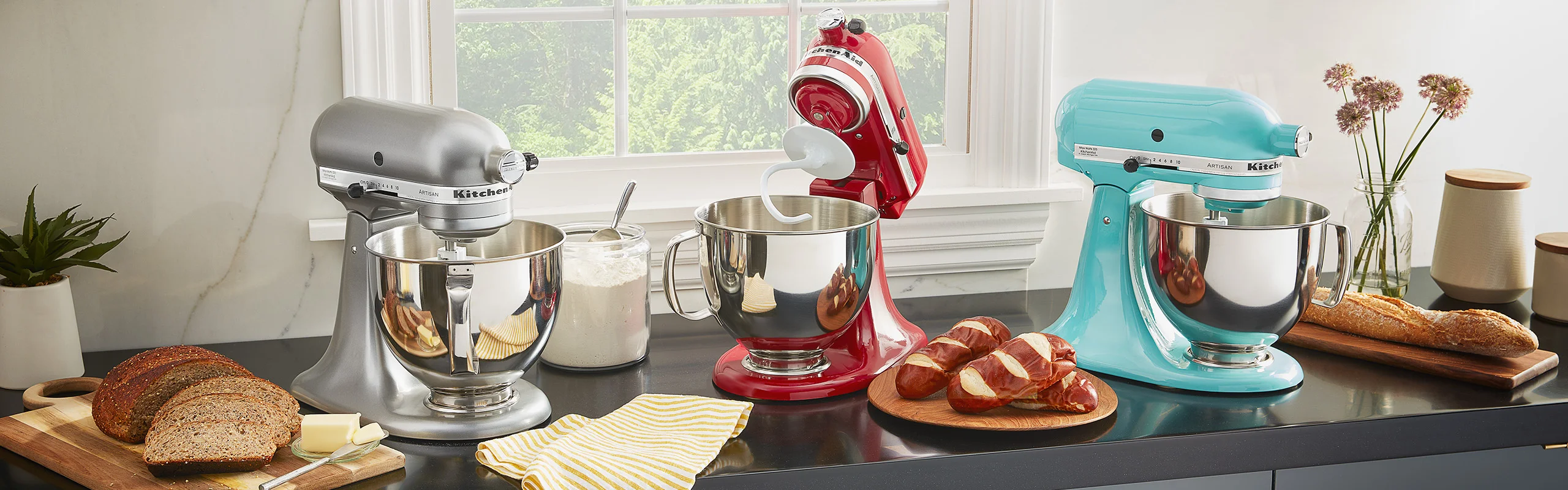Three KitchenAid artisan stand mixers on a countertop in a sunny kitchen